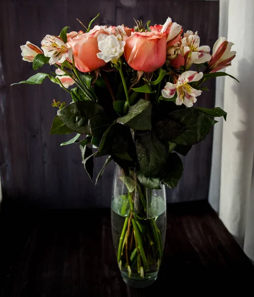 Large luxurious bouquet of peony roses of coral color with white freesia in the noir style in a glass vase on a dark background. dark romance