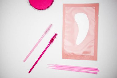 Kirpik uzatmak için araçlar, altın cımbız, mikro fırça, bitmiş bohçalar, pembe fırçalar, göz bantları, beyaz arka plan