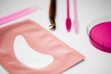 Kirpik uzatmak için araçlar, altın cımbız, mikro fırça, bitmiş bohçalar, pembe fırçalar, göz bantları, beyaz arka plan