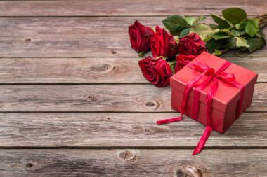 ahşap arka plan üzerinde kırmızı gül buketi ve yayla kırmızı hediye kutusu. Sevgiliye arka plan