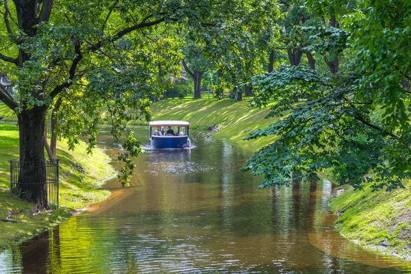 RIGA, Letonia - 7 de agosto de 2017: barco con turistas en el río en el parque de verano cerca del remolque viejo —  Fotos de Stock