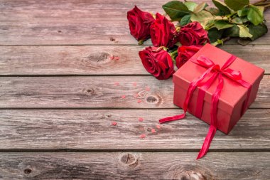 ahşap arka plan üzerinde kırmızı gül buketi ve yayla kırmızı hediye kutusu. Sevgiliye arka plan