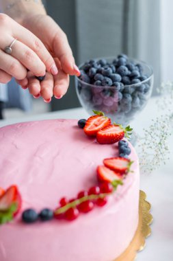 Baker pastaya yabanmersini ekliyor. Doğum günü krem peynirli pembe pasta. Lezzetli pastayı süsleyen kadın