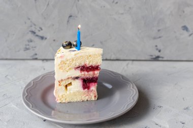 Gri arka planda yanan bir mumla doğum günü pastası dilimi. Kız pastası, fırın ve aşçılık konsepti
