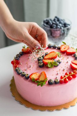 Lezzetli pastayı süsleyen kadın. Çilek, yabanmersini, frenk üzümü ve çiçeklerle süslenmiş ev yapımı pembe doğum günü pastası. Yemek konsepti. Kız doğum günü ya da düğün krem peynir pembe pasta