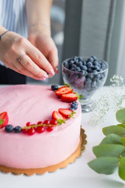 Baker pastaya yabanmersini ekliyor. Doğum günü krem peynirli pembe pasta. Lezzetli pastayı süsleyen kadın