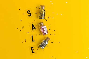 Sarı arka planda siyah harflerle konfeti satılıyor. Düz yatış stili. Konsept özel teklif. Konfetili üç küçük cam şişe.