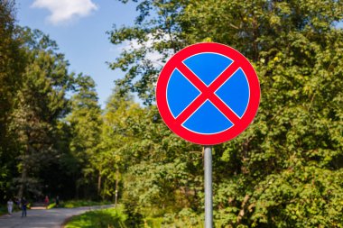 Bulanık yol geçmişinde park levhası yok. Yaz günü. Park arka planında yosunlu metal işareti.
