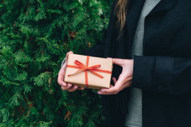 Kahverengi kağıt ve kırmızı kurdeleye sarılı bir kadın yılbaşı ya da doğum günü hediyesi veriyor. Thuja arkaplanı