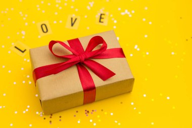 Kırmızı kurdeleli kahverengi hediye kutuları. Aşk kelimesi. Çok renkli konfetiyle sarı arka plan. Düz yatış stili. Anneler günü ya da Sevgililer Günü hediyesi.