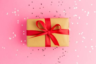Kırmızı kurdeleli kahverengi hediye kutuları. Renkli konfetiyle pembe arka plan. Düz yatış stili. Noel ya da doğum günü hediyesi.