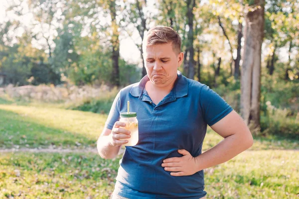 Muž s bolestí břicha. Nešťastný muž venku, ponořený v přírodě, pije sklenici domácí limonády nebo mojito. — Stock fotografie