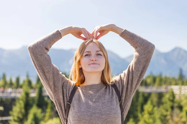 Mädchen Hand, um eine Herzform zu machen. Kopierraum. eine junge hübsche Frau steht auf einem Berg. — Stockfoto