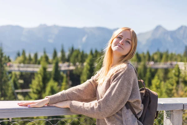 Young woman with backpack standing on cliff's edge. Trekking and tourism concept. Copyspace A young pretty redheaded woman standing on a background of mountains — Stock Photo, Image