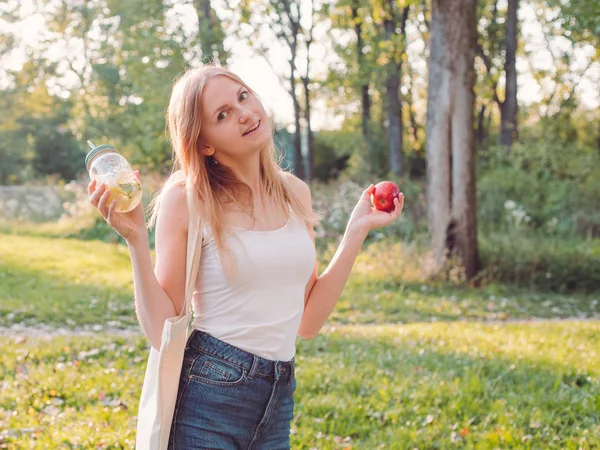 Retrato de niña con manzana roja y limonada. Linda chica hipster en gafas posando para una foto. Concepto ecológico. Al aire libre — Foto de Stock