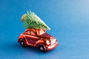 Çatıda Noel ağacı olan kırmızı oyuncak araba, mavi trend arka planı. Yılın rengi