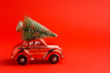 Çatıda Noel ağacı olan kırmızı oyuncak araba, kırmızı trend arka planı. Yeni yıl konsepti