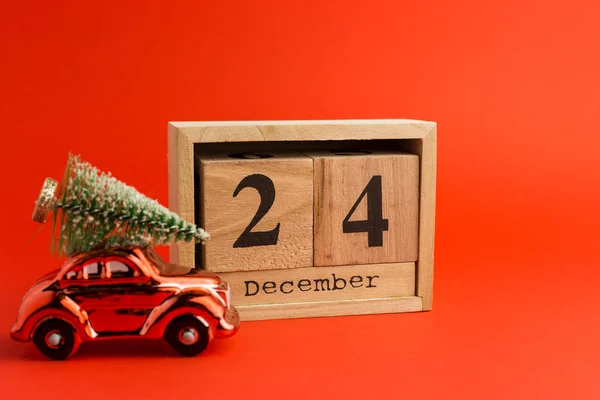 Carro de brinquedo vermelho com uma árvore de Natal no telhado e véspera de Natal Date On Calendar. Dezembro 24, fundo tendência vermelha — Fotografia de Stock