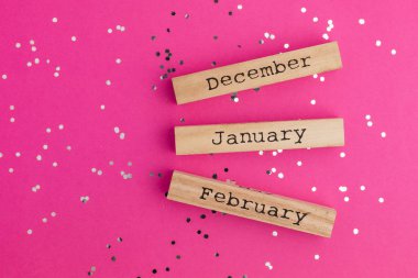 Ahşap takvim, kış ayları Aralık Ocak ayında. Renkli konfetiyle pembe arka plan. Düz yatış stili. Üst görünüm