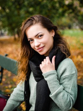 Güzel bir kız bankta oturuyor, güneşli bir sonbahar günü parkta, rahatlatıcı, şık bir şekilde gülümseyen mutlu bir kadının portresi işten sonra ya da çalışmadan sonra.