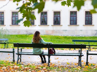 Güzel bir kız bankta oturuyor, güneşli bir sonbahar günü parkta, işten sonra dinleniyor.