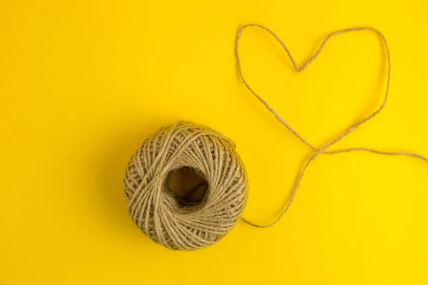 En tråd i form av hjärtat på gul bakgrund. Platt liggstil. Ovanifrån — Stockfoto