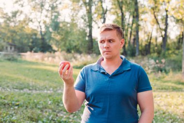 Taze kırmızı elma tutan yakışıklı bir adam, ciddi bir yüz sorgulamayı düşünüyor, kafası çok karışık bir fikir. İnsan Duyguları kavramı