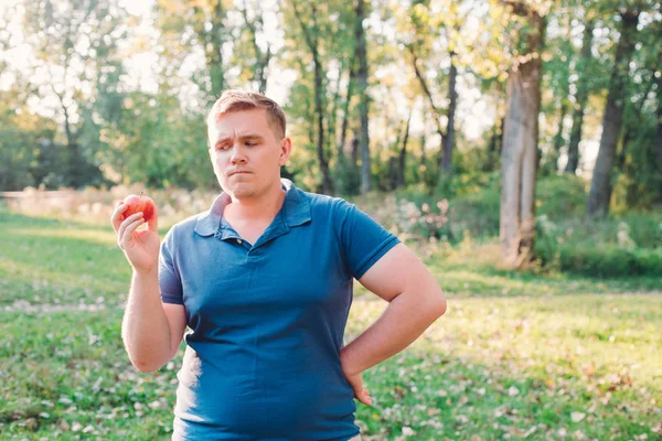 stock image Handsome man holding fresh red apple, serious face thinking about question, very confused idea. Concept of Human Emotions