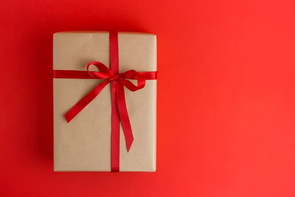 Kırmızı arka planda kırmızı kurdeleli kahverengi hediye kutusu. Düz yatış stili. Noel, tatil ya da doğum günü hediyesi.. Stok Fotoğraf