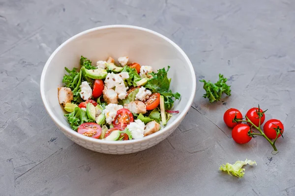 Domates, roka, feta, tavuk göğsü ve avokadodan yapılmış taze salata. Gri arka planda beyaz bir kasede yeni Sezar salatası.
