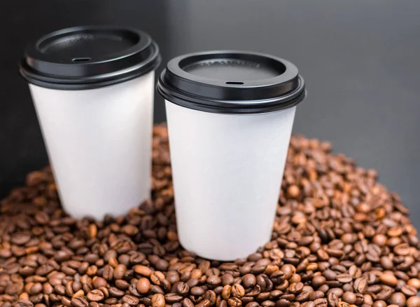 Two White cups of hot coffee on a dark background. Coffee beans background. Vintage style, food banner. Coffee to go in a paper cup, selective focus