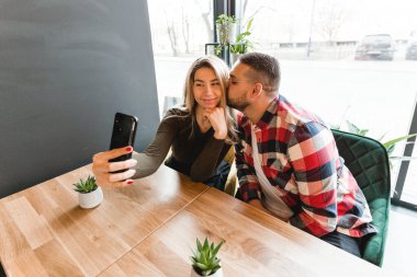 Cafe 'de fotoğraf çeken güzel arkadaşlar. Mutlu genç çift selfie çekiyor, gülümsüyor ve kafede oturuyor.