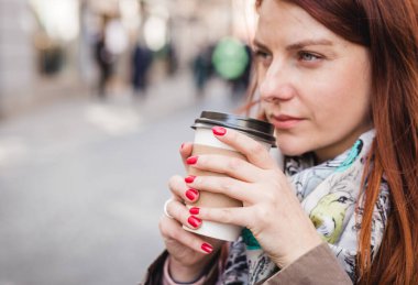 Bulanık sokakta elinde kahve fincanı tutan kadın. Güneşli bir bahar öğleden sonra. Kırmızı manikür.