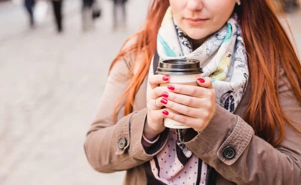 Woman holding coffee cup on the blurred street. Sunny spring afternoon. Red manicure