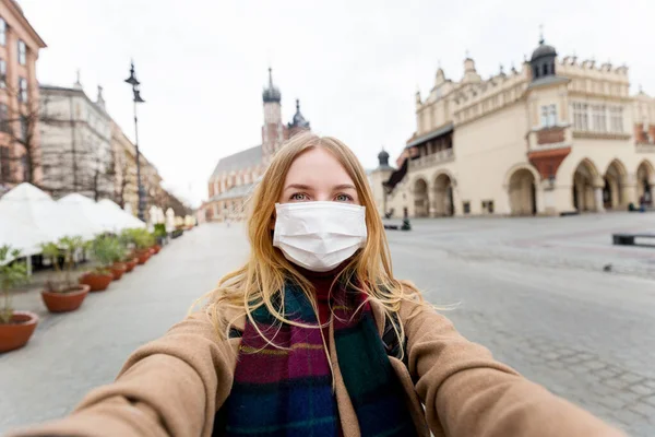 Maskeli şık sarışın kadın Krakow Meydanı 'ndaki ünlü St. Marys Bazilikası' nın önünde selfie çekiyor. Coronavirüs salgını konsepti. Şehirde karantina