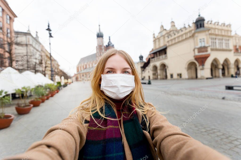 Stylish blonde woman with mask making selfie photo in front of the famous St. Marys Basilica on the Market square Krakow. The concept of the epidemic of the coronavirus. Quarantine in the city