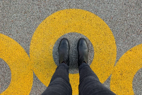 Black shoes standing in yellow circle on the asphalt concrete floor. Comfort zone or frame concept. Feet standing inside circle