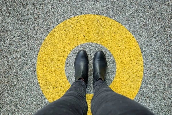 Black shoes standing in yellow circle on the asphalt concrete floor. Comfort zone or frame concept. Feet standing inside circle