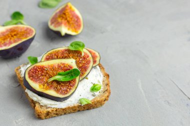 Krem peynirli sandviç, incir, bal ve salata gri arka plandaki ahşap kırsal kesim tahtasında servis ediliyor. Sağlıklı gıda konsepti.