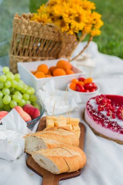 Çiçekli, farklı meyve ve yiyeceklerle dolu piknik sepeti.