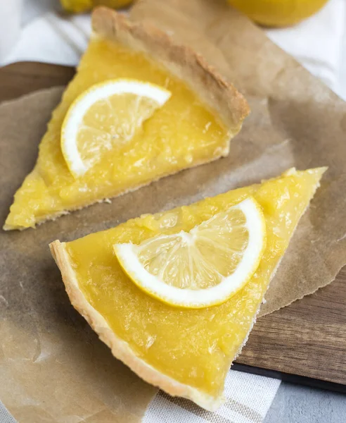two pieces of lemon tart with slice of lemons closeup on stone background