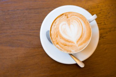 Bir bardak kapuçino ve ahşap arka planda latte sanatı.