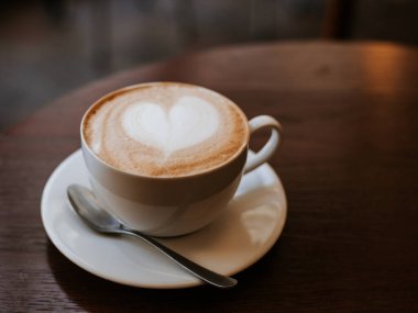 Bir bardak kapuçino ve ahşap arka planda latte sanatı.