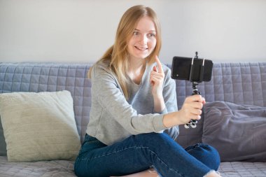 Evde çalışan ve koltukta cep telefonu kullanan bir kadın. Genç blogcu akıllı telefondaki aboneler için içeriği kaydediyor. Kız kayıt günlüğü