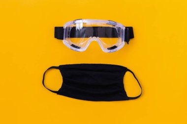 Sarı arka planda Satety gözlükleri olan siyah bez koruyucu maske. Sağlık sigortası Coronavirus karantinası, Hava kirliliği kavramı, düz pankart, üst manzara