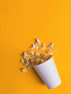 Popcorn in a vase isolated on yellow background. Flat lay banner, top view. To go to the cinema. clipart