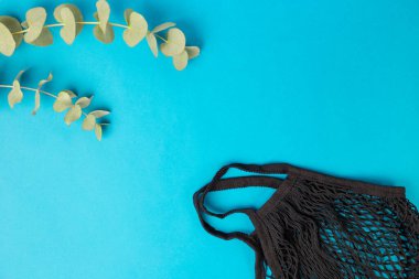 Mavi arka planda yeniden kullanılabilir alışveriş torbası ve okaliptüs yaprakları. Sıfır atık alışveriş kavramı. Plastik yok. Eko sicim siyah çanta. Düz pankart, üst görünüm, boşluğu kopyala