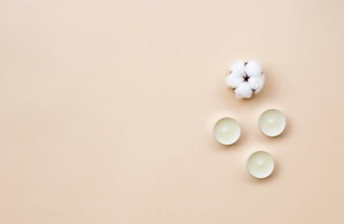 Minimum spa tedavisi bileşimi. Beyaz aroma mumları, açık bej arka planda pamuk topağı.