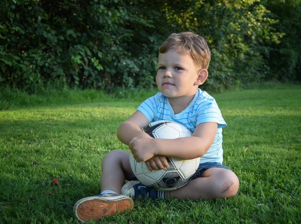 Menino com bola de futebol sentado na grama — Fotografia de Stock