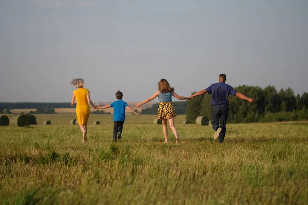Mom, dad, son and daughter running across the field — Stock Photo, Image